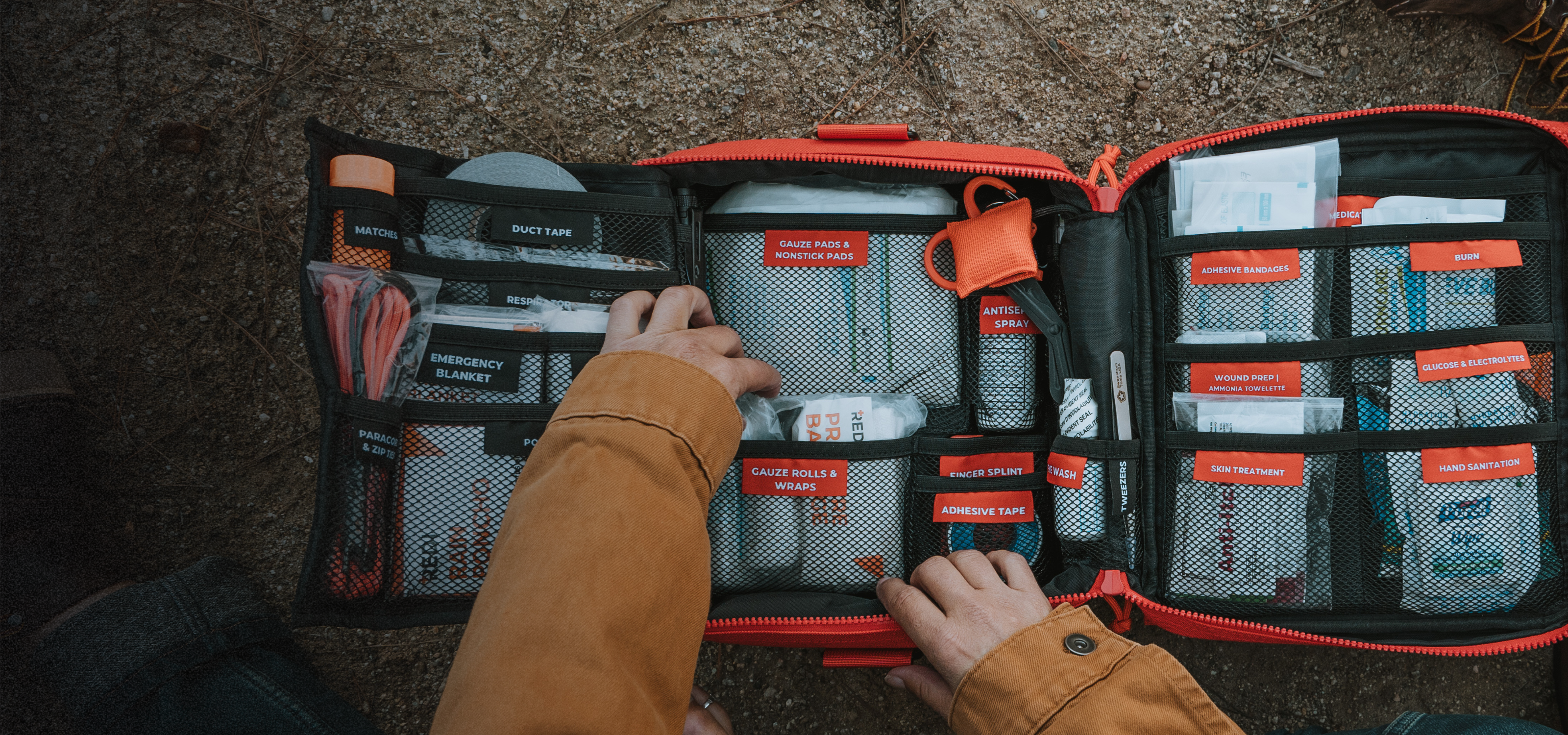 A photo of the Roadie open, its labeled pouches for each first aid item, and hands digging in to grab gauze rolls.