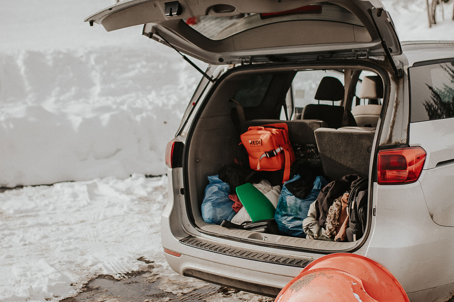 The Roadie first aid kit attached to the back seat of a van with the velcro mounting pad, with ski clothes and sleds in the back at a snowy location. 